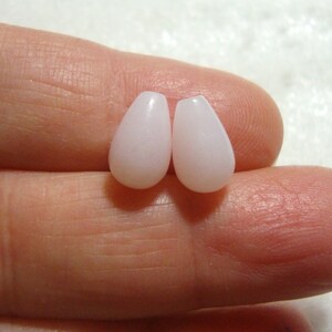 May include: Two teardrop-shaped beads in a pale pink colour. The beads are smooth and glossy.