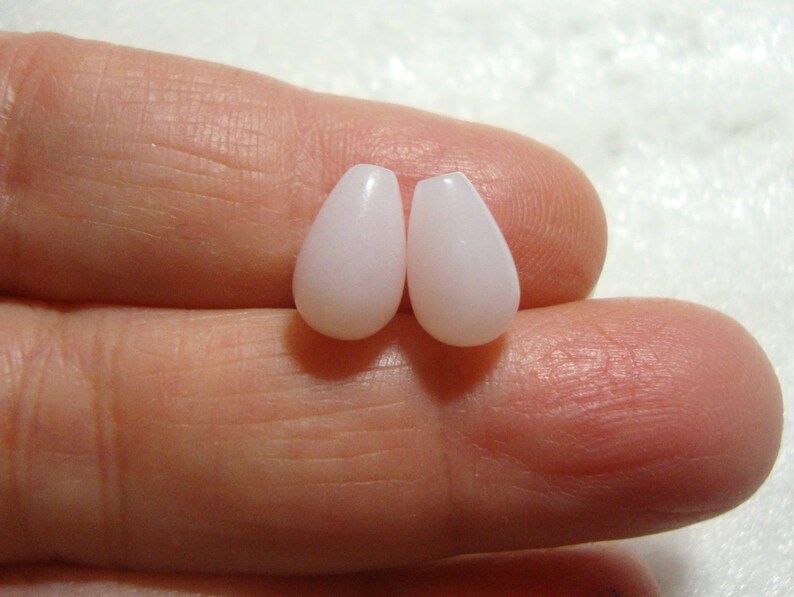 May include: Two teardrop-shaped beads in a pale pink colour. The beads are smooth and glossy.