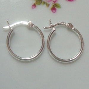 May include: A pair of silver hoop earrings with a hinged closure. The earrings are simple and elegant.