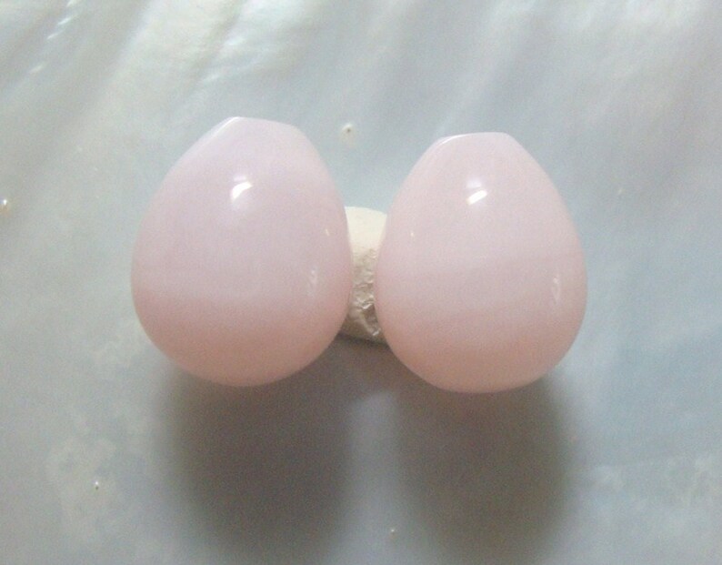 Puede incluir: Dos cuentas de color rosa p&aacute;lido en forma de l&aacute;grima.