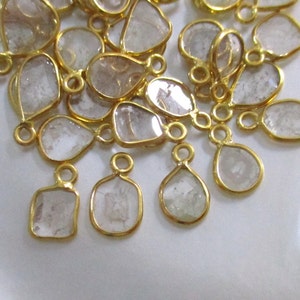 May include: A group of clear, faceted, teardrop-shaped gemstone pendants with gold-toned metal settings and jump rings.