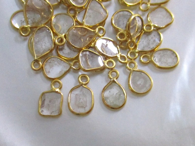 May include: A group of clear, faceted, teardrop-shaped gemstone pendants with gold-toned metal settings and jump rings.