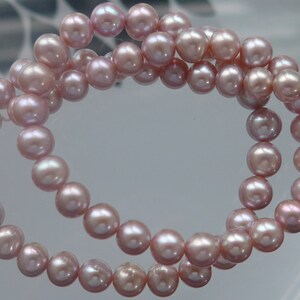 May include: A strand of pink freshwater pearls, strung on a white thread. The pearls are round and have a slight iridescent sheen.