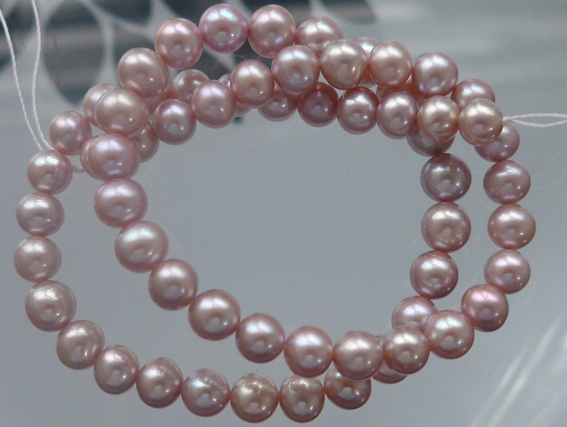 May include: A strand of pink freshwater pearls, strung on a white thread. The pearls are round and have a slight iridescent sheen.