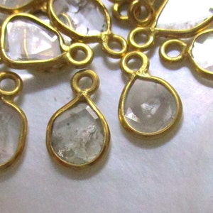 May include: A group of gold-toned metal charms with clear faceted glass stones. The charms are shaped like teardrops and ovals.