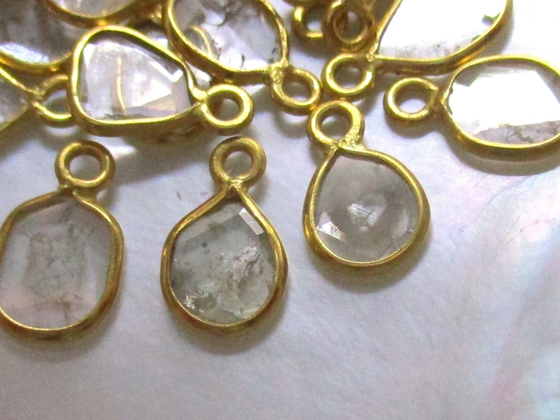 May include: A group of gold-toned metal charms with clear faceted glass stones. The charms are shaped like teardrops and ovals.
