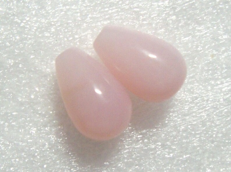 May include: Two teardrop-shaped pink opal beads. The beads are smooth and have a glossy finish.
