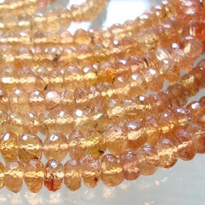May include: A strand of faceted, translucent, orange-brown gemstone beads. The beads are round and have a slightly irregular shape. The beads are strung on a clear thread.
