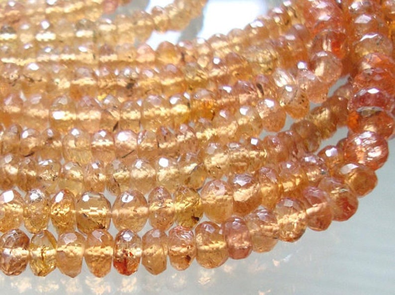 May include: A strand of faceted, translucent, orange-brown gemstone beads. The beads are round and have a slightly irregular shape. The beads are strung on a clear thread.
