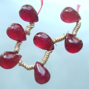 May include: A strand of red gemstone beads strung on gold wire. The beads are teardrop shaped and have a glossy finish.