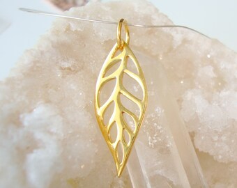 May include: A gold-colored leaf pendant with intricate cut-out details. The pendant is suspended from a small loop at the top, suggesting it's designed to be worn as a necklace. The leaf shape is elongated and features a detailed vein pattern.