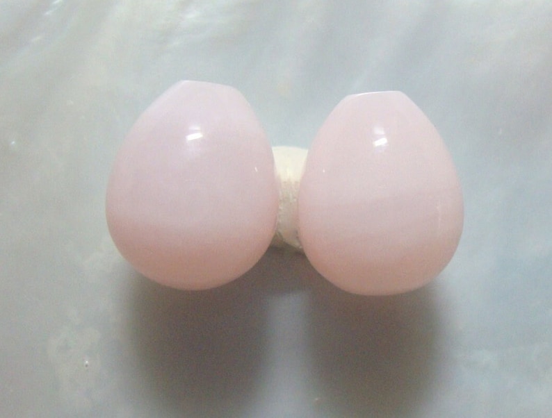 Puede incluir: Dos cuentas de vidrio redondas, lisas y pulidas, de color rosa.