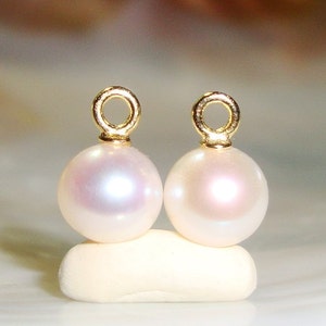 May include: Two white pearl earrings with gold jump rings. The pearls are round and smooth.