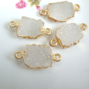 May include: Four white quartz crystal connector charms with gold-toned metal loops. The charms are irregular in shape and have a sparkly, textured surface.