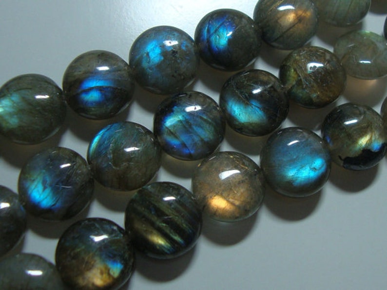 May include: A strand of round, iridescent labradorite beads with a blue-green sheen. The beads are smooth and polished, and they have a natural, organic look.