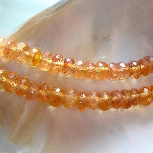 May include: A strand of orange sunstone beads. The beads are faceted and have a slightly irregular shape. The beads are strung on a clear thread.