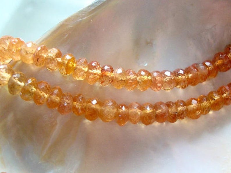 May include: A strand of orange sunstone beads. The beads are faceted and have a slightly irregular shape. The beads are strung on a clear thread.