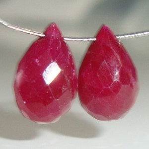 May include: Two teardrop-shaped ruby red gemstone beads strung on a silver wire.
