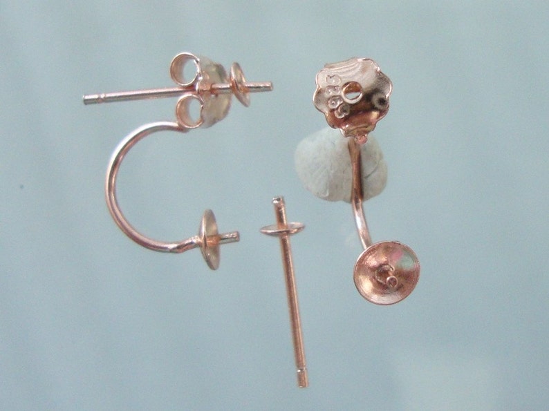 May include: A pair of rose gold earring findings with a curved post and a flat back. The findings are designed to hold a pearl or other gemstone.