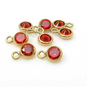 May include: A group of seven red rhinestone charms with gold-toned jump rings. The rhinestones are round and have a faceted design.