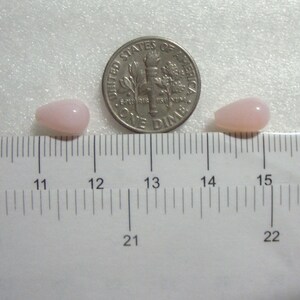 May include: Two pink teardrop-shaped beads next to a US dime coin on a white ruler. The beads are approximately 2.5 cm long.