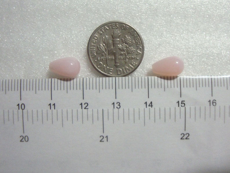 May include: Two pink teardrop-shaped beads next to a US dime coin on a white ruler. The beads are approximately 2.5 cm long.