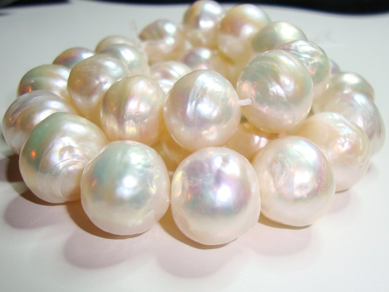 May include: A strand of white pearls with a pearlescent sheen. The pearls are round and smooth, and they are arranged in a loose, flowing pattern.