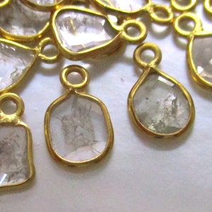 May include: A group of gold-toned pendants with clear, faceted gemstones. The pendants are in various shapes, including teardrop, square, and rectangular.
