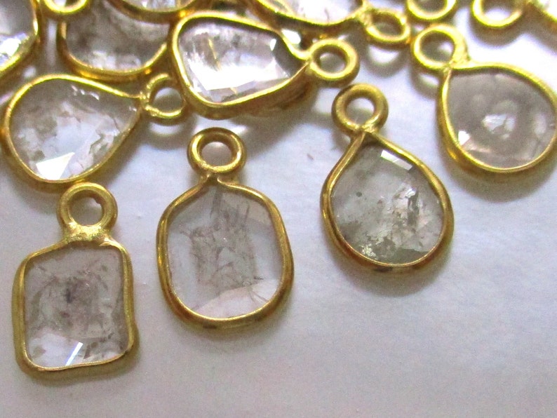 May include: A group of gold-toned pendants with clear, faceted gemstones. The pendants are in various shapes, including teardrop, square, and rectangular.