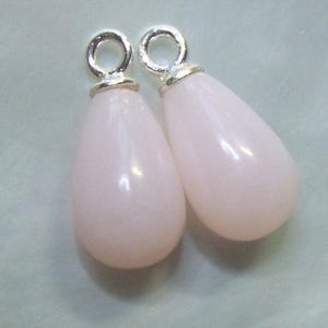 May include: Two teardrop-shaped pink opal pendants with silver jump rings. The pendants are approximately 2.5 cm long.
