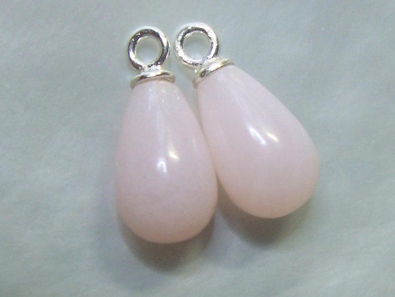 May include: Two teardrop-shaped pink opal pendants with silver jump rings. The pendants are approximately 2.5 cm long.