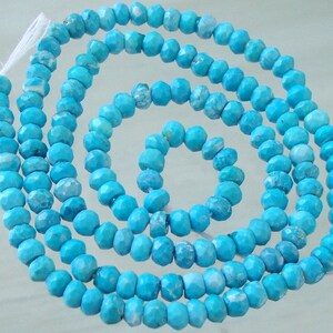 May include: A strand of turquoise blue gemstone beads. The beads are faceted and have a slightly irregular shape. The beads are strung on a white thread.