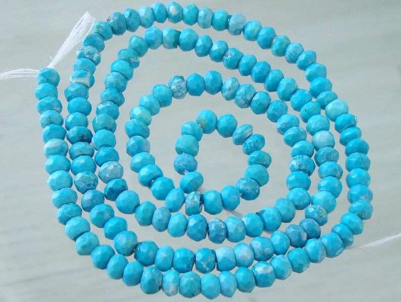 May include: A strand of turquoise blue gemstone beads. The beads are faceted and have a slightly irregular shape. The beads are strung on a white thread.