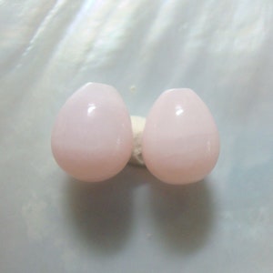 Puede incluir: Dos cuentas de color rosa en forma de l&aacute;grima con un acabado liso y brillante.