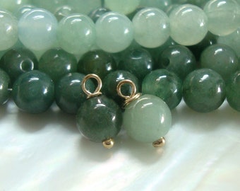 May include: Two green jade beads with gold-toned loops. The beads are round and smooth, and the loops are attached to the top of the beads.
