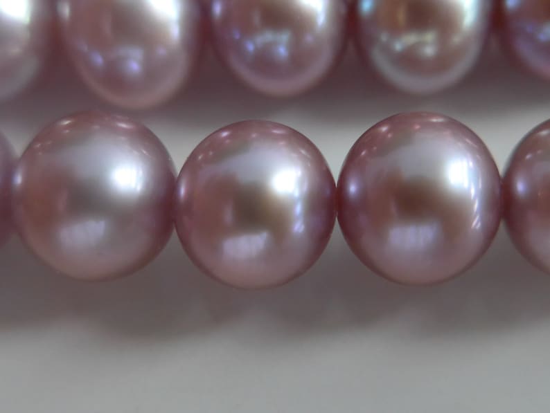 May include: A strand of iridescent pink pearls. The pearls are round and smooth, with a high lustre.