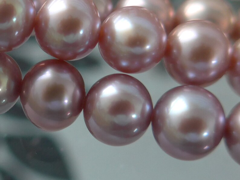 May include: A strand of pink pearls with a high lustre. The pearls are round and smooth, and they are strung together on a clear thread.