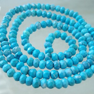 May include: A strand of turquoise blue gemstone beads. The beads are faceted and have a slightly irregular shape. The beads are strung on a clear thread.