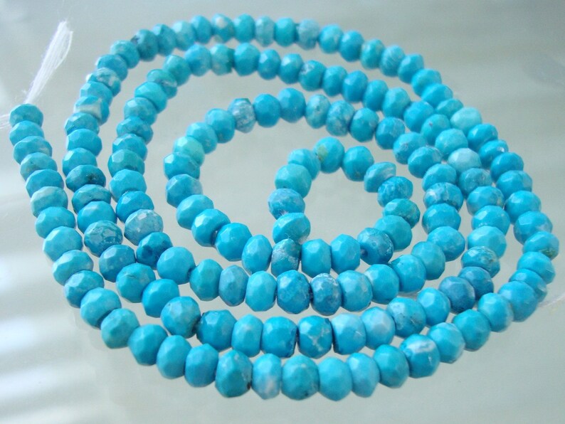 May include: A strand of turquoise blue gemstone beads. The beads are faceted and have a slightly irregular shape. The beads are strung on a clear thread.