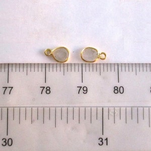 May include: Two gold-toned metal teardrop-shaped pendants with clear glass inserts. The pendants are measured against a ruler, with the top of the pendants aligned with the 78 and 79 markings.