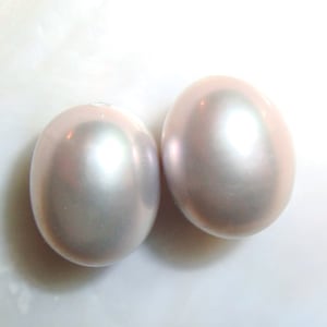 May include: Two large, oval-shaped, iridescent pearls with a light pink hue.