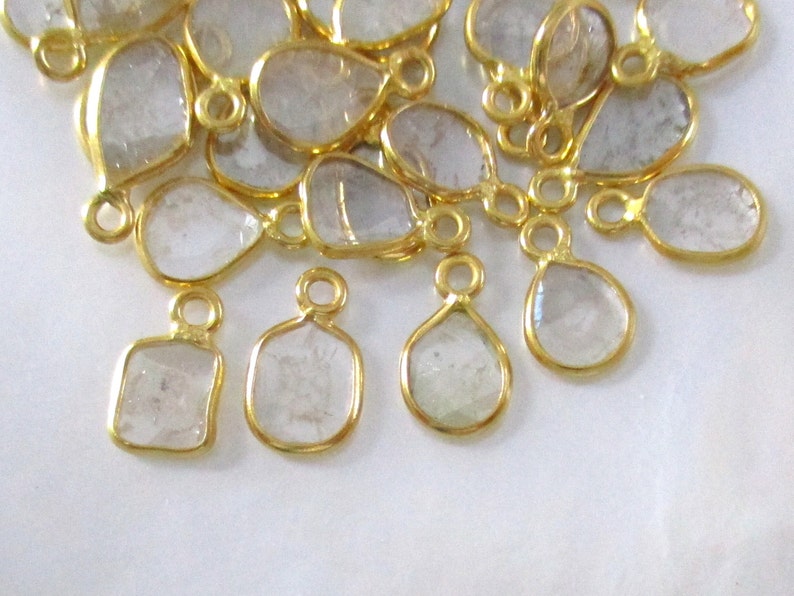 May include: A group of gold-plated, clear glass teardrop and square-shaped charms with a loop for hanging.