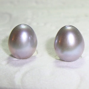 May include: Two lustrous, oval-shaped pearls. The pearls have a gradient of colours, transitioning from a soft lavender at the base to a silvery-white at the top. Each pearl has a small hole at the top.