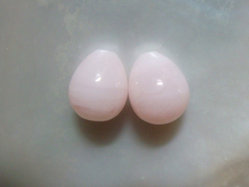 Puede incluir: Dos cuentas de color rosa en forma de l&aacute;grima, cada una con un acabado liso y brillante.