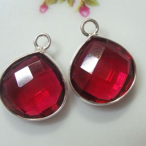 May include: Two silver pendant charms with red faceted glass drops. The drops are teardrop shaped and have a shiny finish.