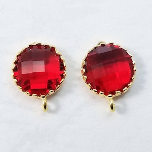 May include: Two gold-toned round pendant charms with red faceted glass stones. Each charm has a loop at the bottom.