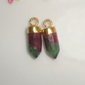 May include: Two gold-capped pendants with green and pink gemstone drops. The gemstones are faceted and have a pointed shape.