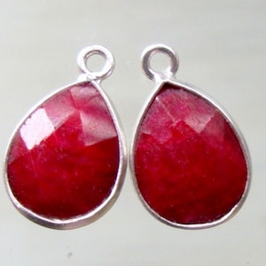May include: Two teardrop-shaped red gemstone pendants with silver settings. The gemstones are faceted and have a shiny finish.