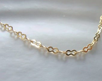 Op de afbeelding: Een gouden ketting met een delicaat, gekoppeld ontwerp. Elke schakel is in de vorm van een acht.