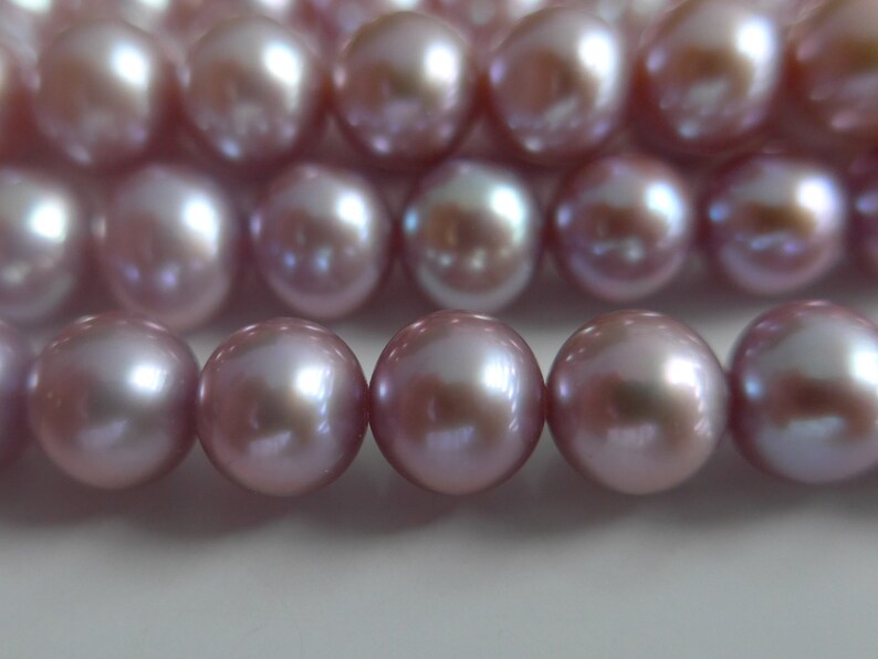 May include: A strand of lavender-coloured pearls, each pearl is smooth and round, with a subtle iridescent sheen.